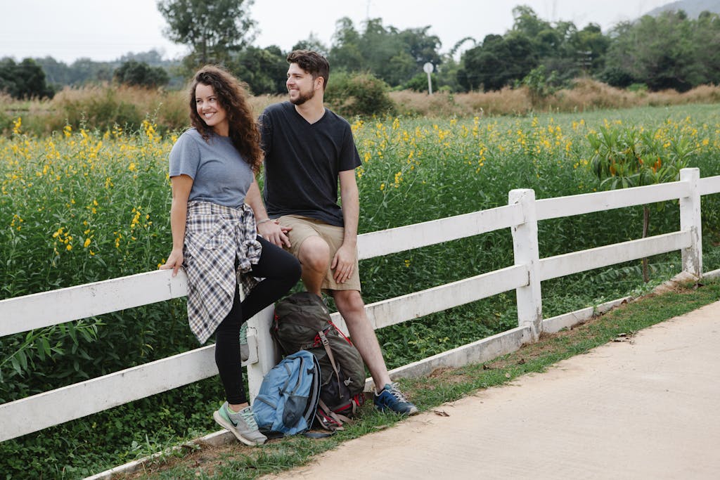 A happy couple relaxing by a fence in a meadow, enjoying a warm summer day.